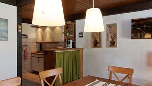 Ein Essbereich mit einem Holztisch, Stühlen und einer grünen Tischläufer. Im Hintergrund ist eine Küche mit gefliestem Rücksprühefeld und Holzschränken zu sehen.