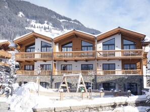 Un hotel de varios pisos con balcones de madera y cimientos de piedra, con una imponente montaña nevada de fondo.