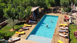 A rectangular swimming pool with a wooden deck, surrounded by lounge chairs and tables, and shaded by trees. - Holiday Home in Corsica Near the Beach (Poggio-Mezzana)