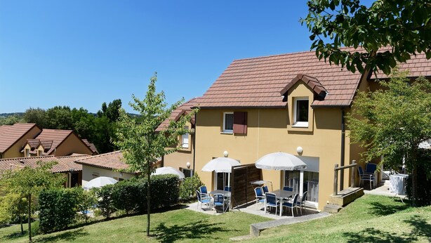 A two-story building with a brown roof, a patio with tables and chairs, and a small garden area. - Holiday Home in Sarlat Near Castelnaud Castle (Sarlat-la-Canéda)