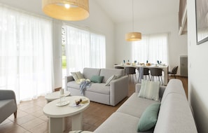 A modern living room with a sofa, a dining table, and a kitchen area in the background.