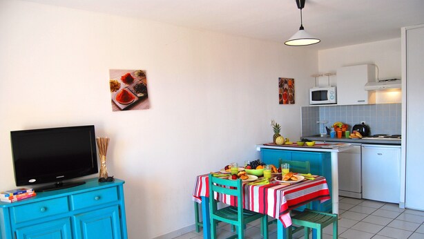 A compact kitchen with a dining area, a TV on a cabinet, and a microwave above the counter. - Sunny Apartment for Groups (Cerbère)