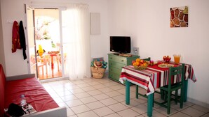 A small, bright room with a red sofa, a dining table with a red and white tablecloth, and a television on a green cabinet. - Sunny Apartment for Groups (Cerbère)