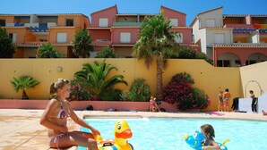 A swimming pool area with a yellow wall, palm trees, and a building with balconies in the background. - Sunny Apartment for Groups (Cerbère)