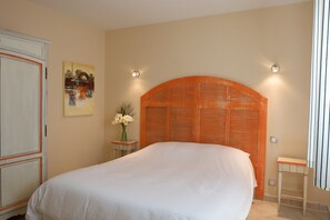 A bedroom with a large bed, a wooden headboard, a nightstand with a vase of flowers, and a wall-mounted light fixture. - Villa in Callian With Private Pool (Callian)