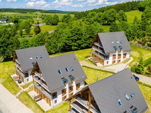 A modern multi-story building with a sloped roof, surrounded by lush greenery and rolling hills. - Spacious, Modern Apartment Near the Centre (Winterberg)