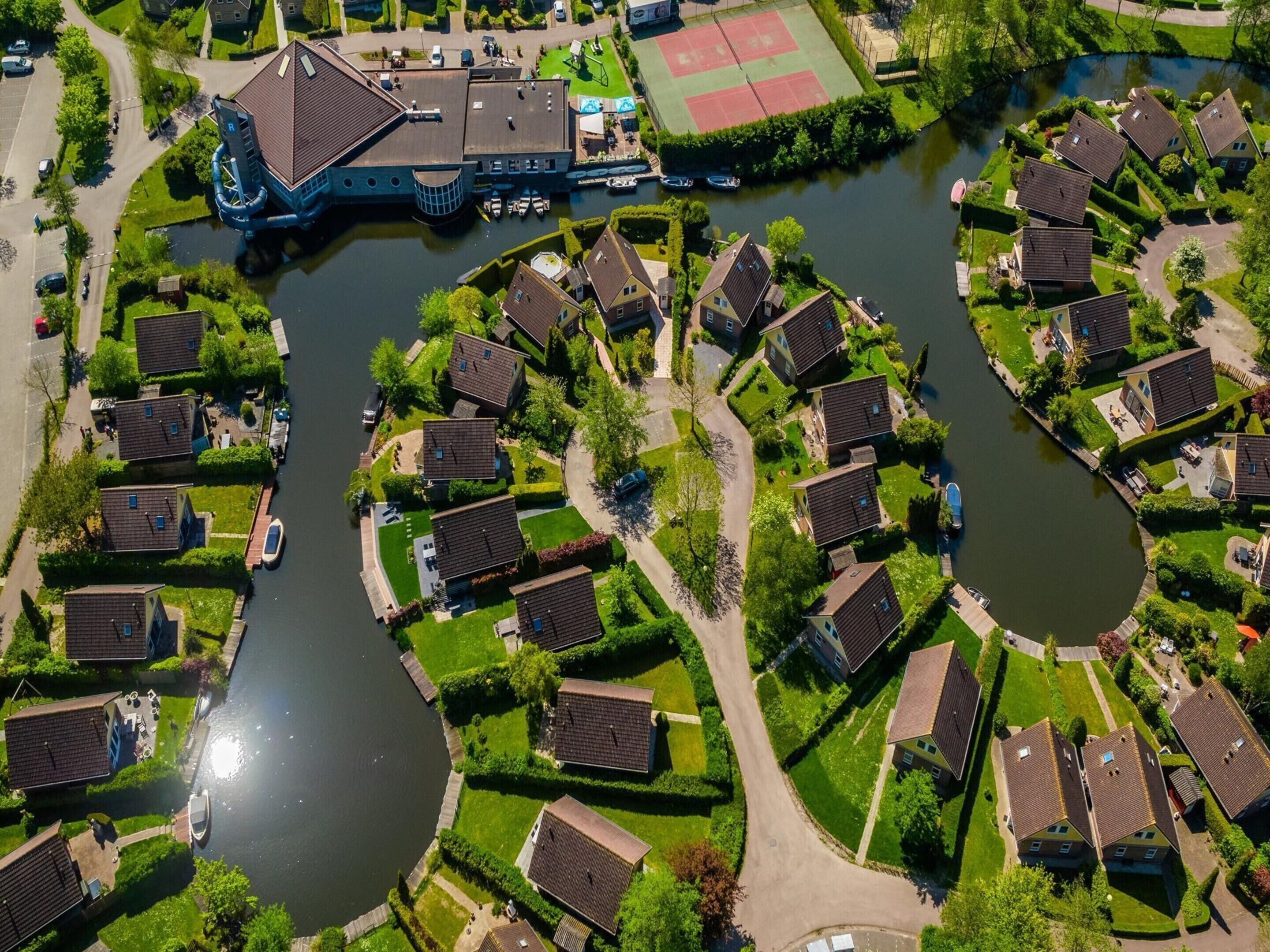 Vista aérea de una zona residencial con casas ubicadas alrededor de un canal, que incluye un campo deportivo y un edificio grande con un techo distintivo.