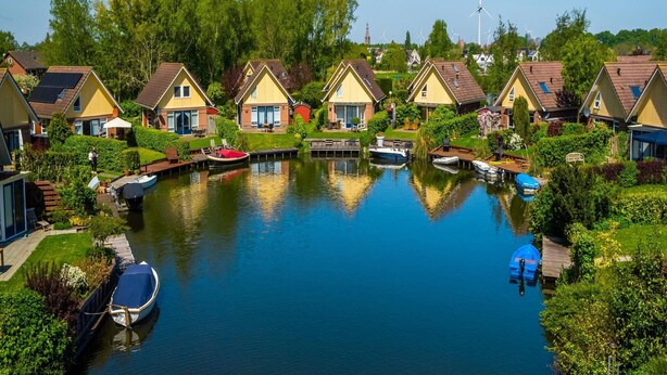 A canal with houses on one side and wind turbines in the background. - Beautiful House With Sauna Near Ijsselmeer (Medemblik)