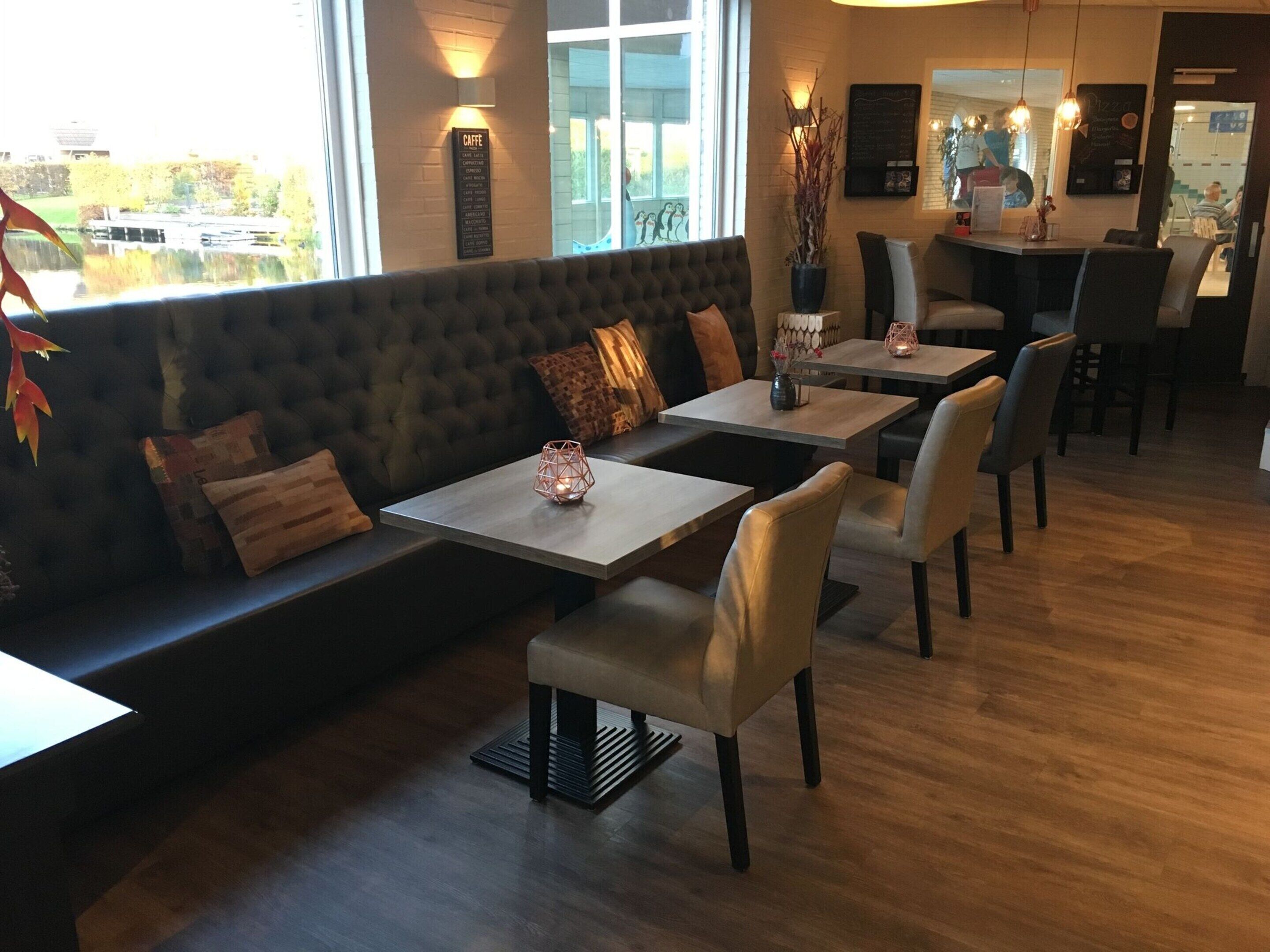 A cozy restaurant with a dark upholstered bench, wooden tables, and chairs.