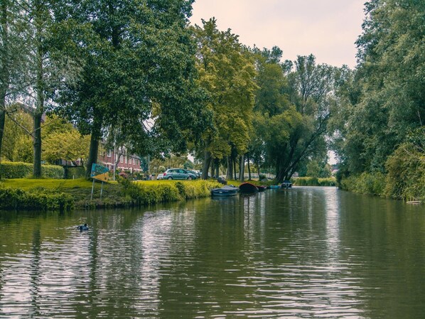 Une rivière paisible où naviguent des bateaux, bordée d’arbres luxuriants et enjambée par un pont.