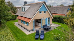 Una casa con techo inclinado, un garaje pequeño adosado y un patio con dos sillones.