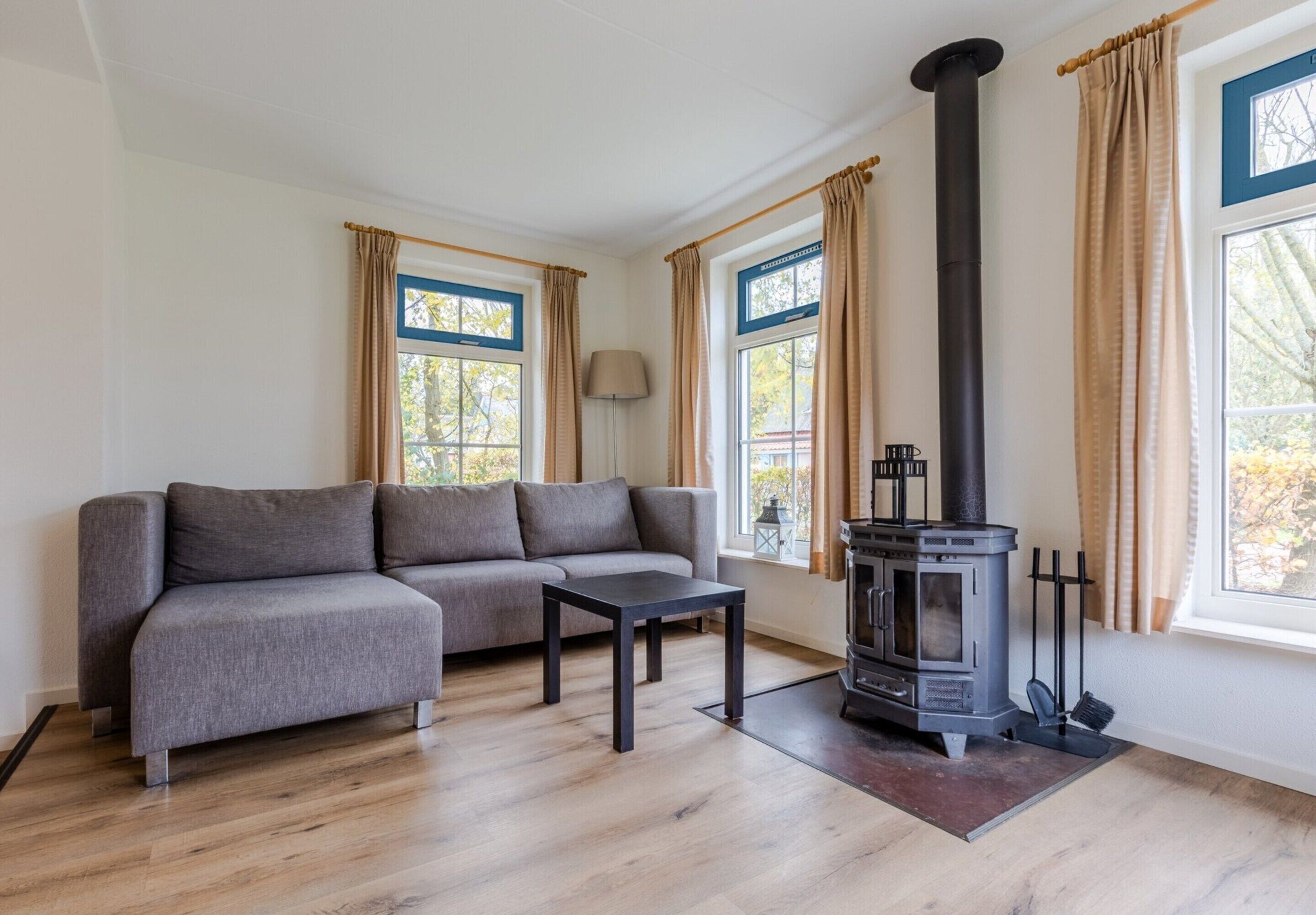 A modern living room with a grey sofa, a small black table, and a wood-burning stove.