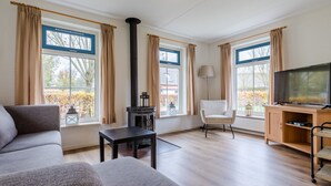 Una sala de estar con un sofá, una mesa, una silla, un televisor, una chimenea y una ventana con cortinas.