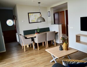 A modern kitchen with a dining area, wooden flooring, and a mounted television. - Bungalow in 's-gravenzande With Nautical Charm ('s-Gravenzande)
