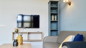 Ett modernt vardagsrum med en platt-TV som är monterad på väggen, ett träbord som används som soffbord och som är dekorerat med olika föremål, en grå soffa med mönstrade kuddar och en blå hyllsektion.