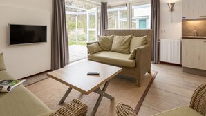 A modern living room with a sofa, a coffee table, a TV, and a kitchen area. - Luxury Chalet With two Bathrooms, Near the sSa on Texel (De Koog)