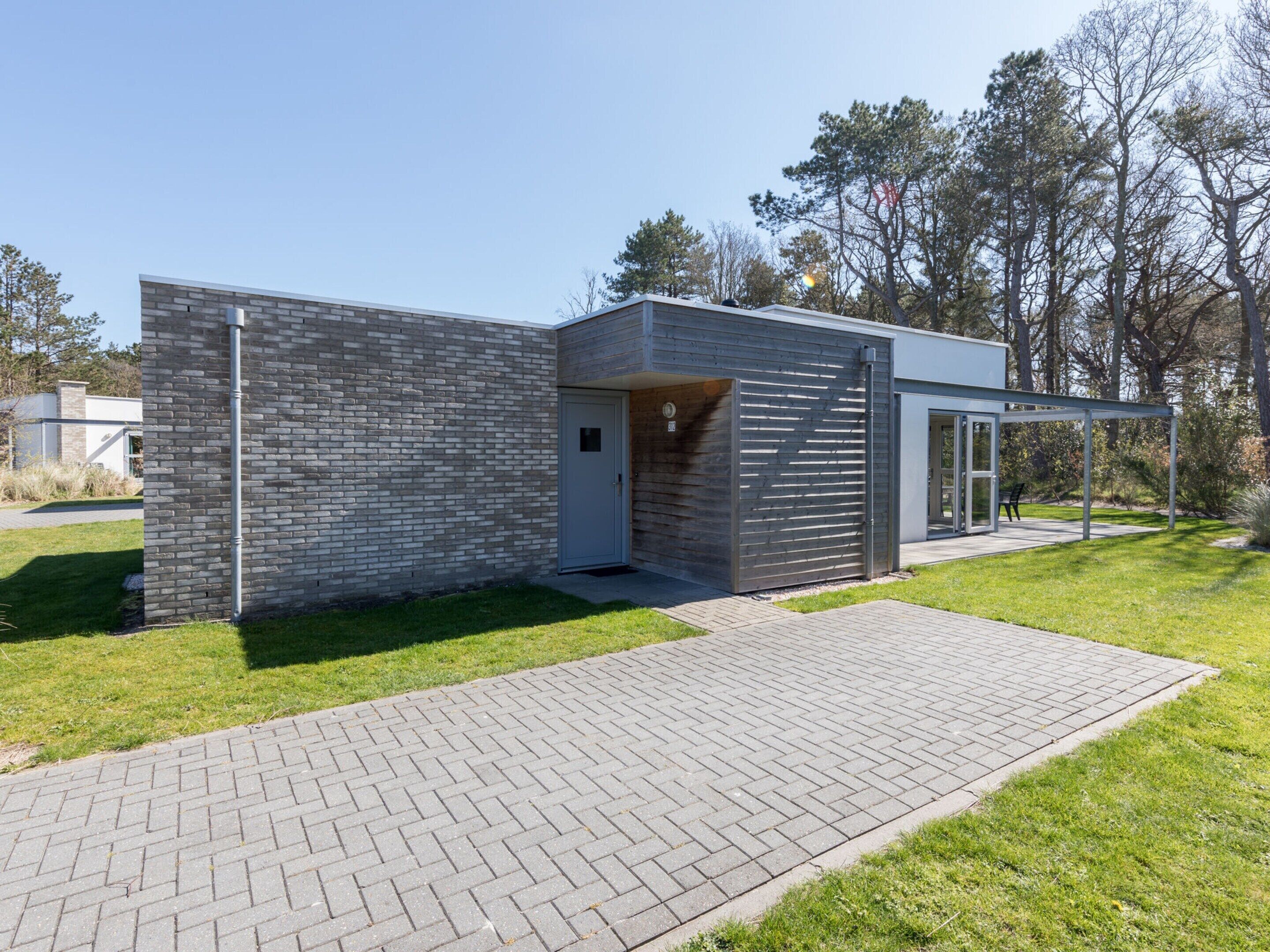 Un bâtiment moderne avec une façade en briques, un porche et un chemin pavé menant à une porte.