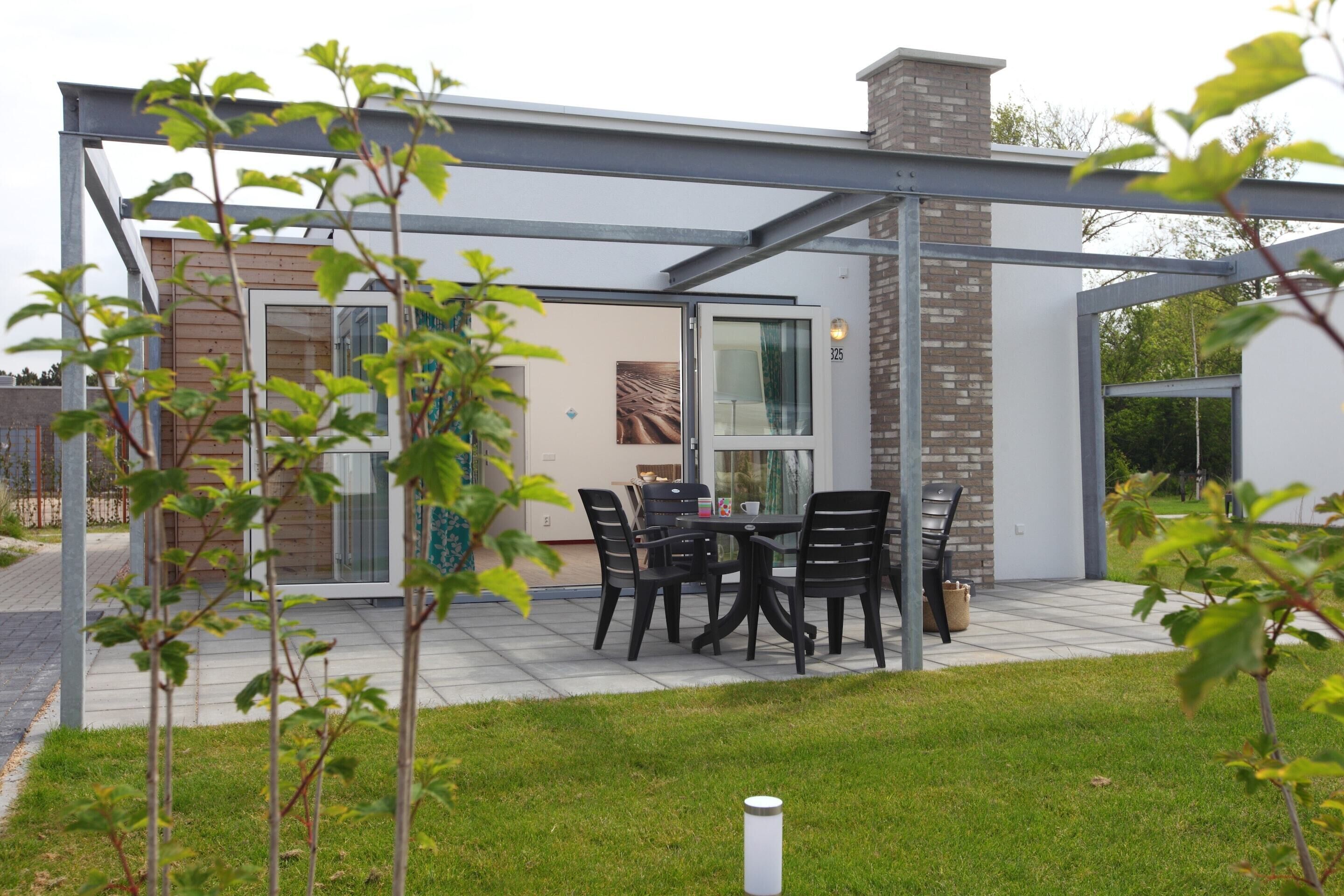 A modern outdoor patio with a table and chairs, a glass door, and a brick chimney.