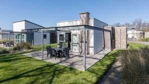 A modern outdoor patio area with a table and chairs, surrounded by a glass enclosure. - Luxury Chalet With two Bathrooms, Near the sSa on Texel (De Koog)