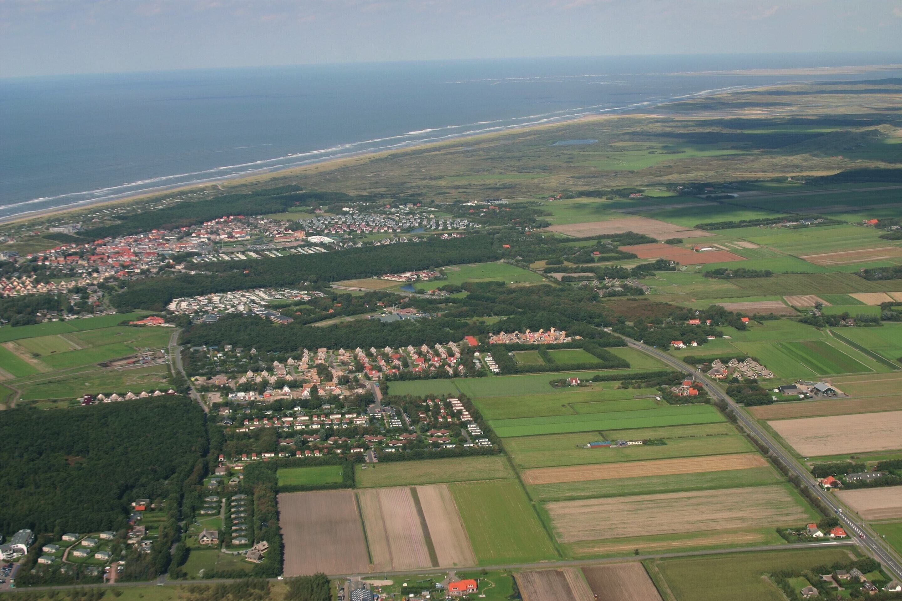 Egy tengerparti város légi felvételén lakóövezetek, mezők és egy strand láthatók.