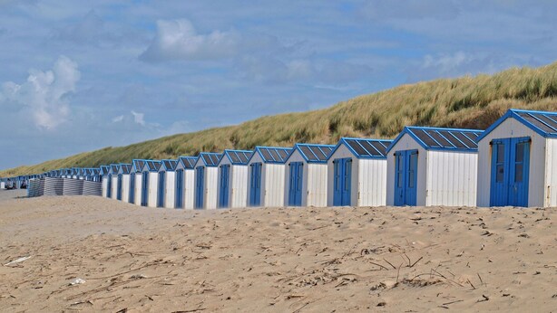 A row of beach huts with blue doors and white walls, lined up along a sandy beach with dunes in the background. - Luxury Chalet With two Bathrooms, Near the sSa on Texel (De Koog)