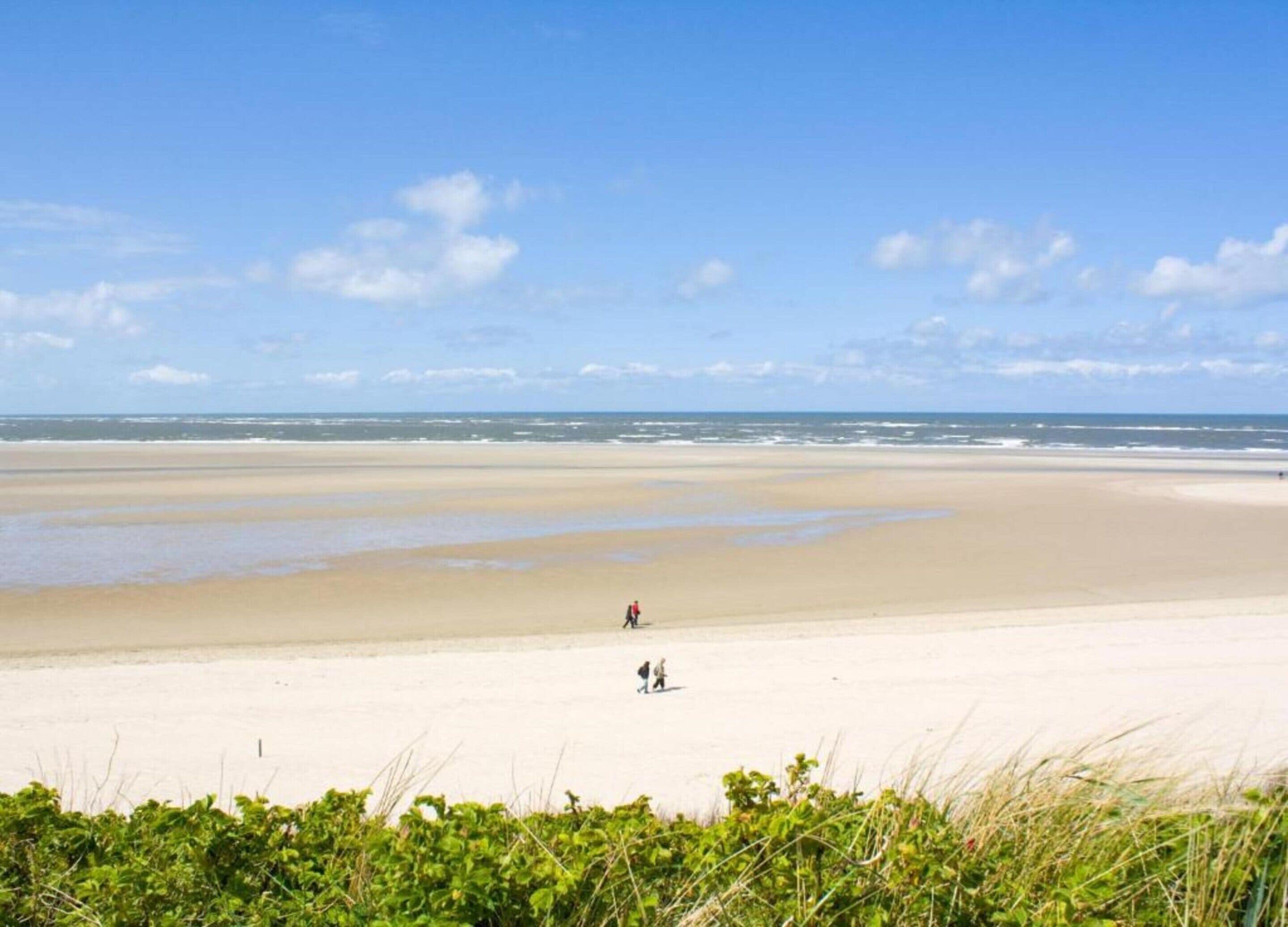 A wide sandy beach with a clear sky and a few people walking.