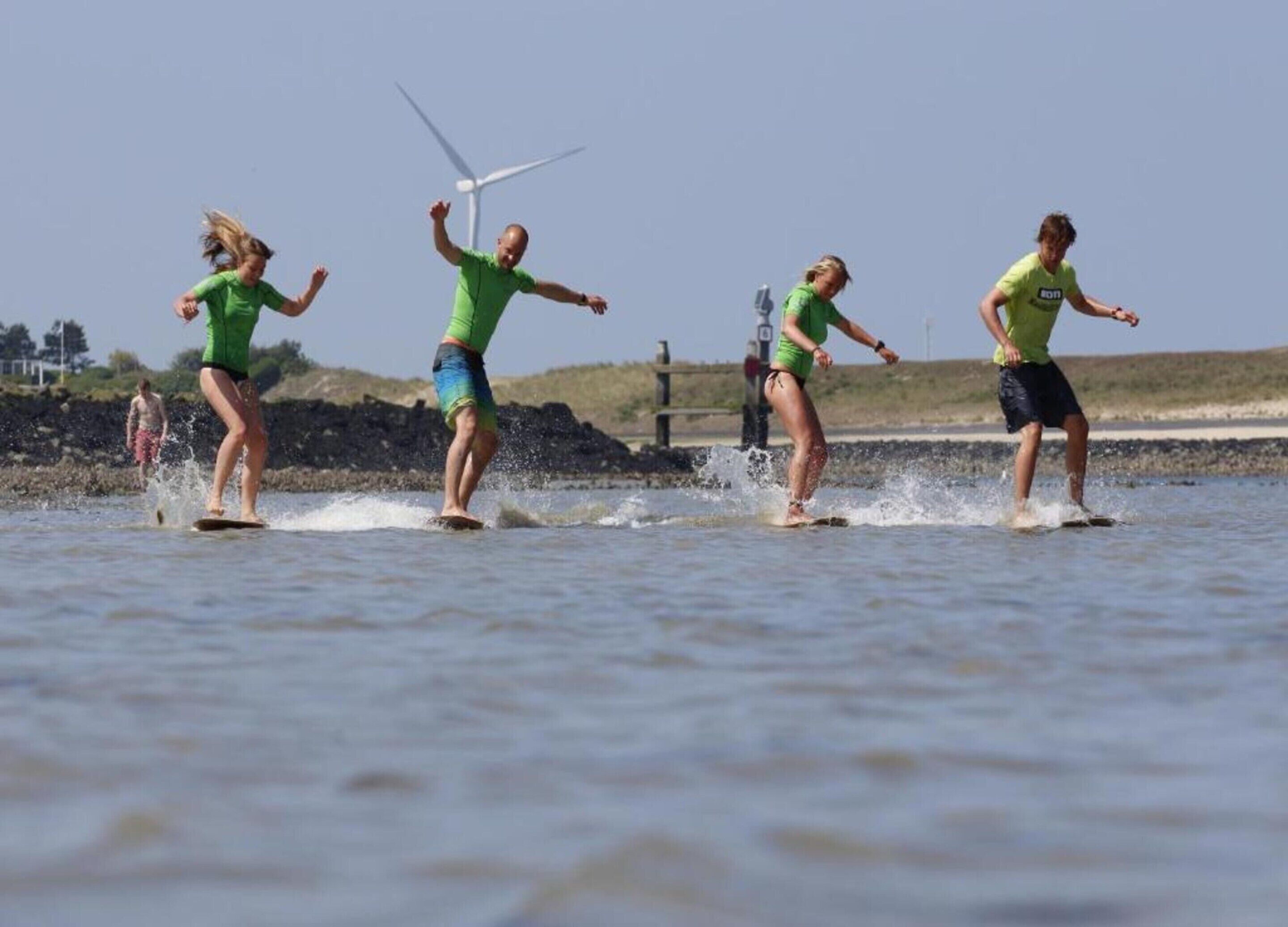 Four people windsurfing on a body of water with a wind turbine in the background.