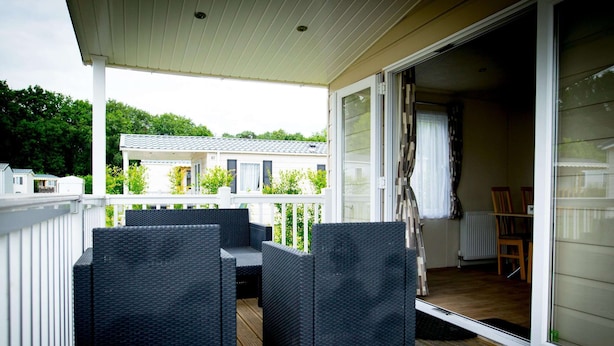 A covered outdoor area with wicker furniture, a sliding glass door, and a view of a house in the background. - Chalet Near Loonse and Drunense Dunes (Udenhout)