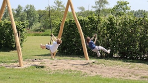 A swing set in an outdoor area with a grassy field and trees in the background. - Chalet Near Loonse and Drunense Dunes (Udenhout)