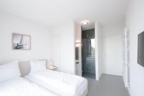 A modern bedroom with a bed, a bedside table, a framed picture, a walk-in closet, and a shower area. - Villa Oesterdam Comfort 8 Persons (Tholen)