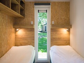 Ein Zimmer mit zwei Betten, Holzwänden und einem Fenster mit Blick auf eine Grünfläche und ein Gebäude.