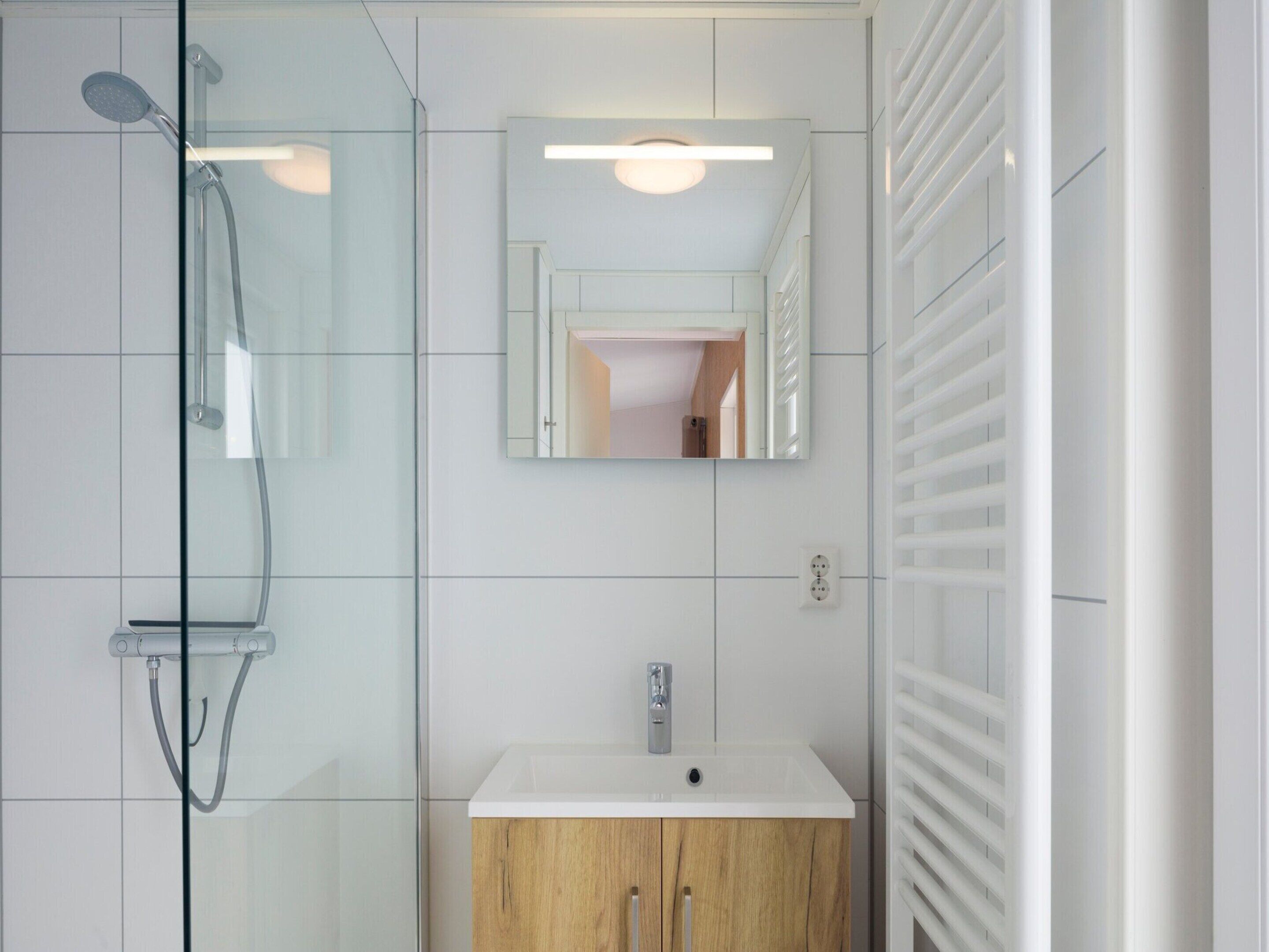 A modern bathroom with a glass-enclosed shower, a white sink, and a wooden cabinet.