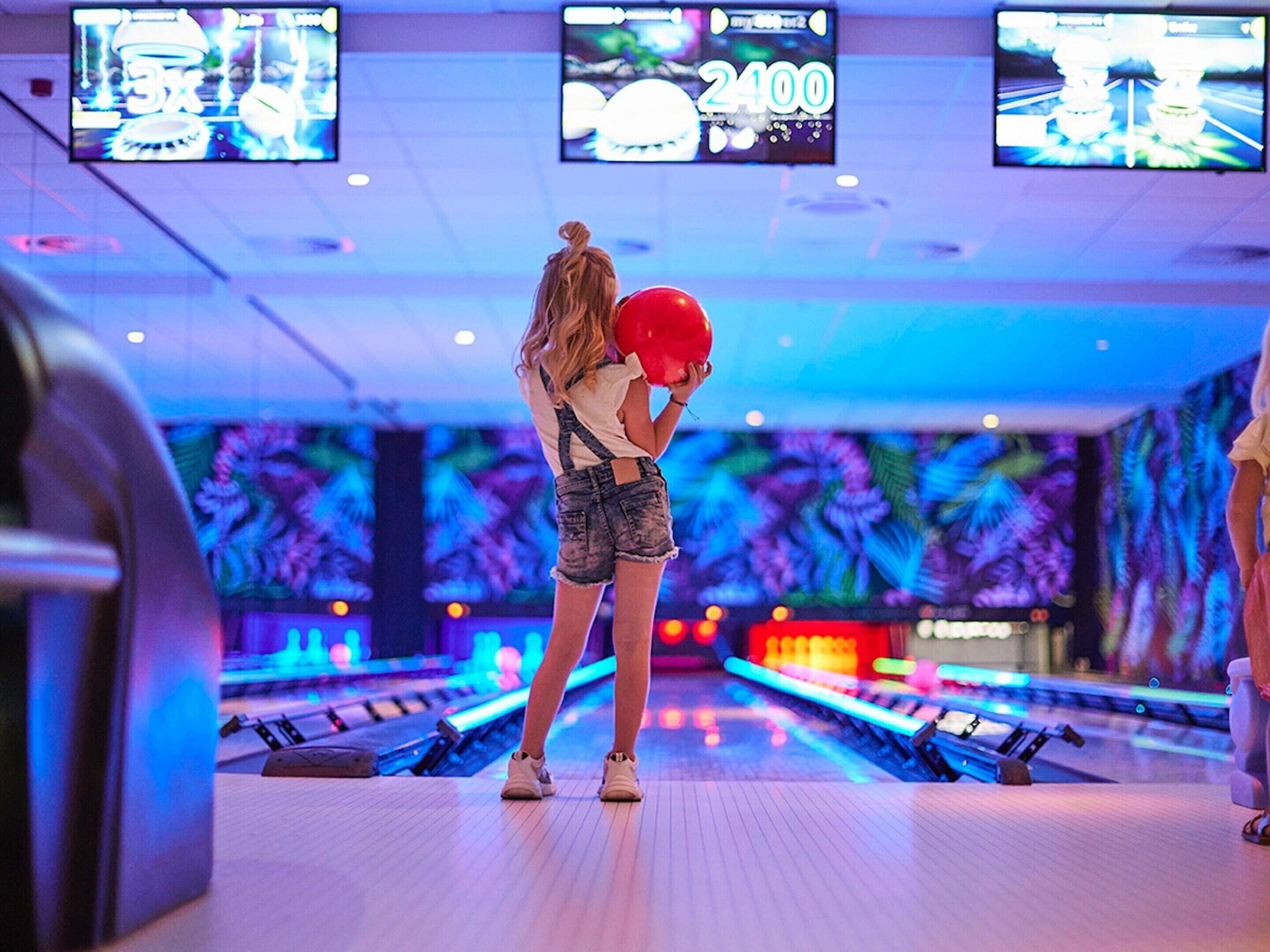 Een bowlinghal met meerdere banen, een scorebord en een muur met neonverlichting.