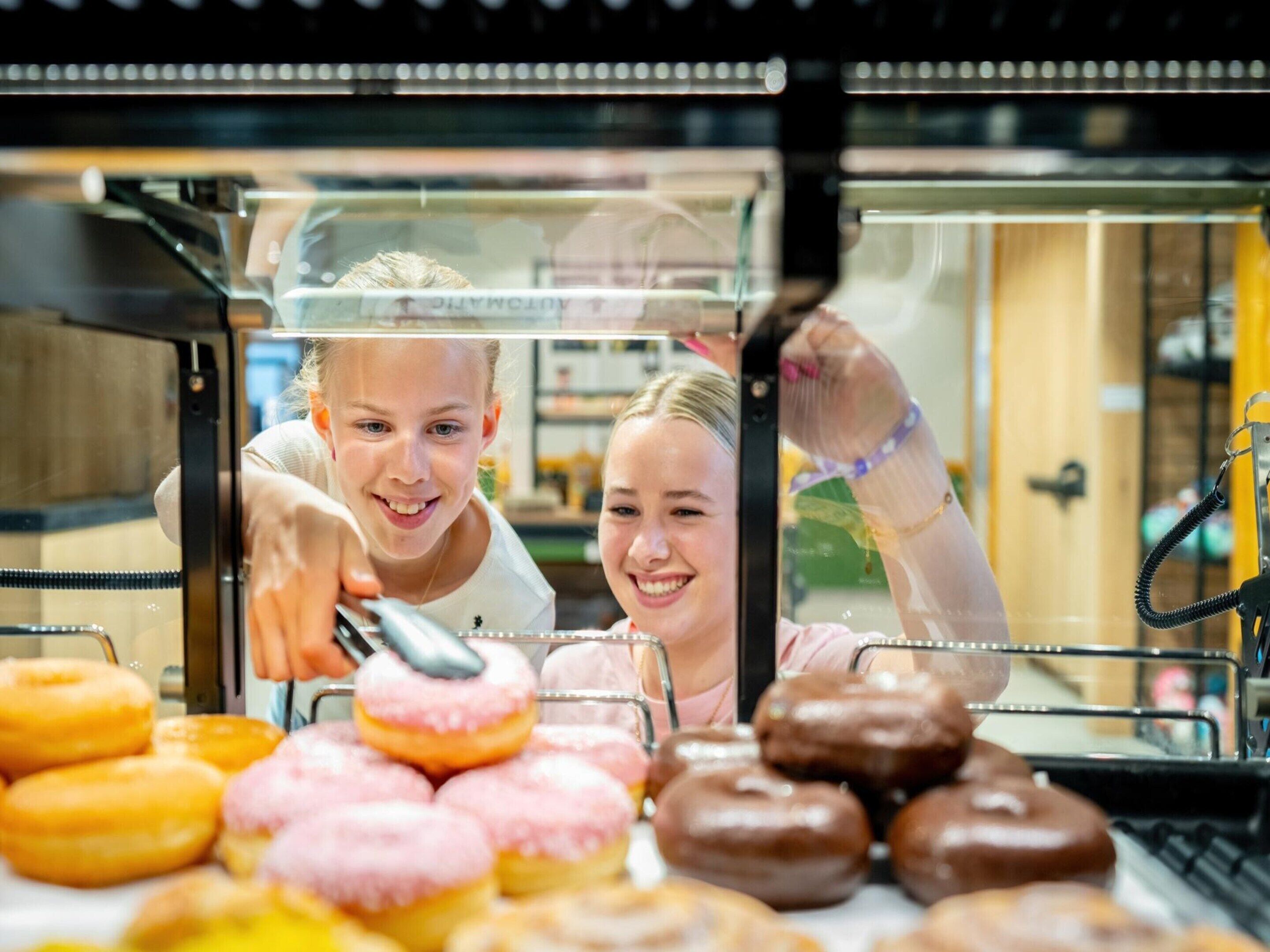 Vitrine com donuts de vários sabores e uma pessoa esticando a mão para pegar um.