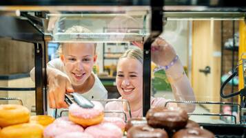 Vitrine com donuts de vários sabores e uma pessoa esticando a mão para pegar um.