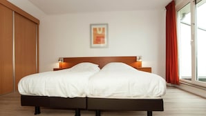 Un lit double avec une tête de lit en bois, deux lampes de chevet et une grande fenêtre avec des rideaux.