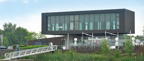 A modern building with a flat roof, large windows, and a bridge leading to it.