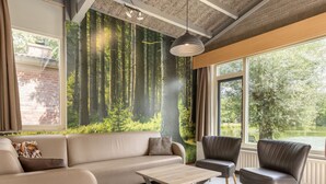 Un soggiorno moderno con un divano, un tavolino e due poltrone. Un'ampia finestra offre vista su una foresta e un lago.