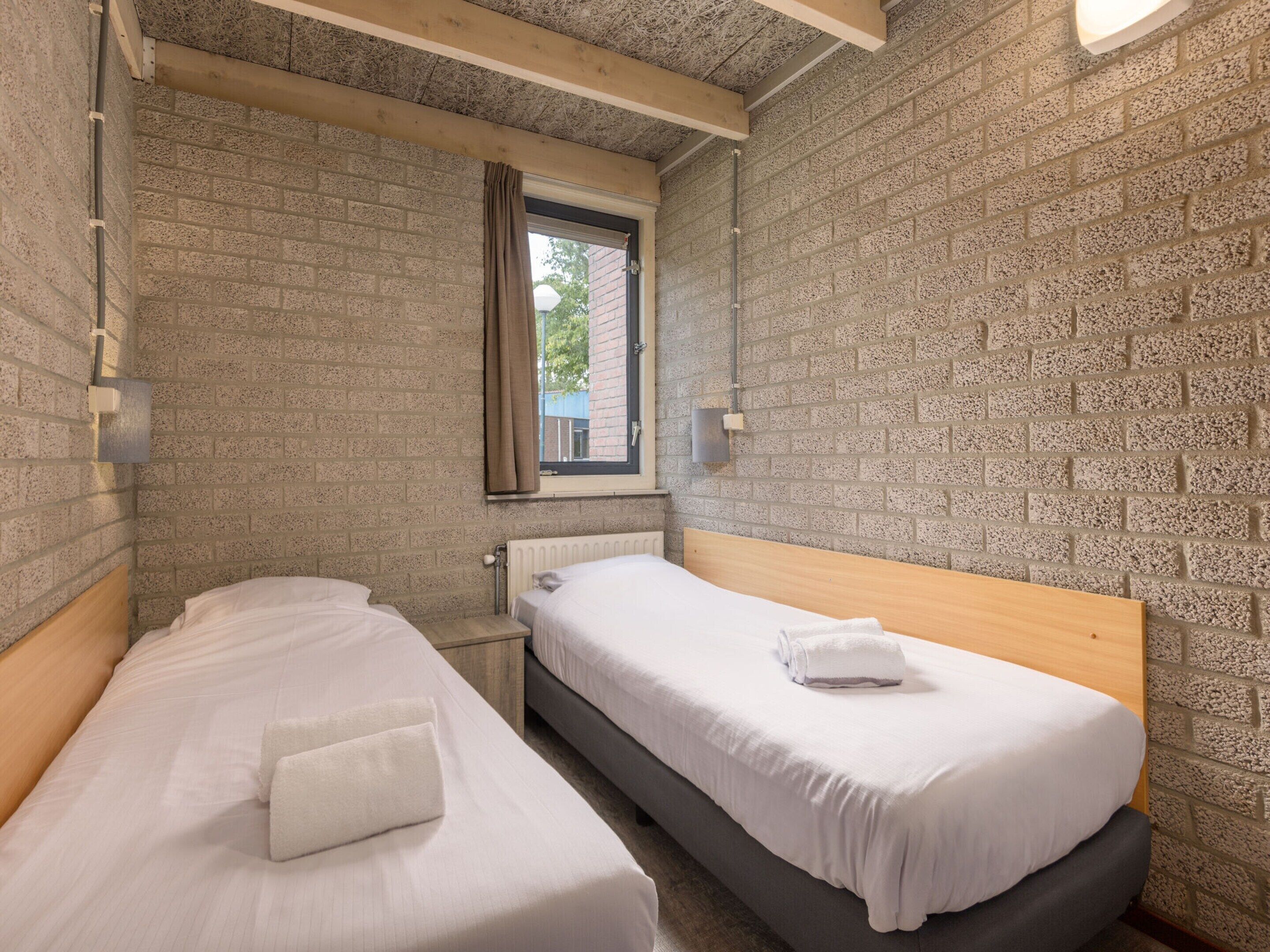 A small, compact bedroom with two single beds, a window with a view of the outside, and a brick wall.