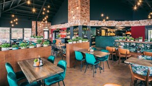 Interno di un ristorante con soffitti alti, pareti in mattoni a vista e lampade pendenti. Tavoli e sedie disposti per la ristorazione.