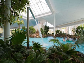 An indoor swimming pool with a waterfall feature, surrounded by tropical plants and a glass ceiling. - Nice, Child-friendly Villa With a Sauna in Limburg (Roggel)