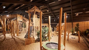 Una struttura di legno con parete da arrampicata e altalene in un’area interna sabbiosa.