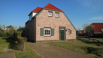 A brick house with a red roof, a green door, and a small porch.