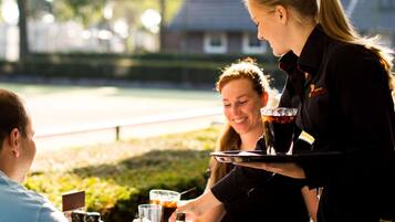 A person serving drinks at an outdoor table with a glass of beer and a bottle of Amstel beer.