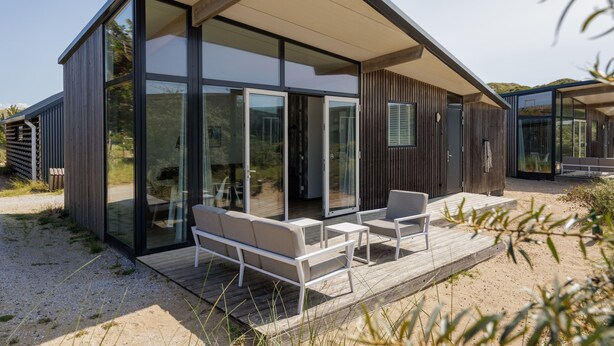 A modern house with large glass doors, a wooden deck, and outdoor seating. - Bloemendaal Beach Escape (Overveen)