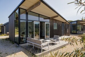 Une maison moderne dotée de grandes portes vitrées, d’une terrasse en bois et d’un espace salon extérieur.