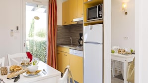 A compact kitchen with a microwave, refrigerator, and a dining area with a table set for two. - Holiday Park in Corsica With Terrace Homes (Belgodere)