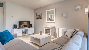 A modern living room with a sofa, coffee table, TV, and fireplace.