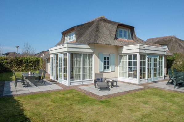 A house with a large glass conservatory, a dining area with outdoor furniture, and a well-maintained lawn.