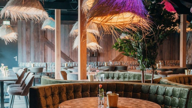 A restaurant with round tables and cushioned booths, featuring thatched umbrellas and wooden walls. - Well Furnished Tent Lodge with Terrace near Veluwe (Voorthuizen)